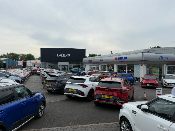Car dealership with Suzuki and Kia signage and a variety of parked cars.