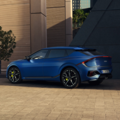 Blue car parked, rear and side view, against urban architecture.