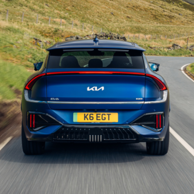 Blue Kia EV6 driving on winding rural road.