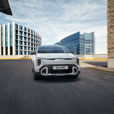 White car with number plate K14 HPC driving on urban road with modern buildings.