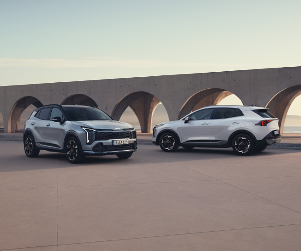 Two white cars parked side by side next to a concrete structure with arches.