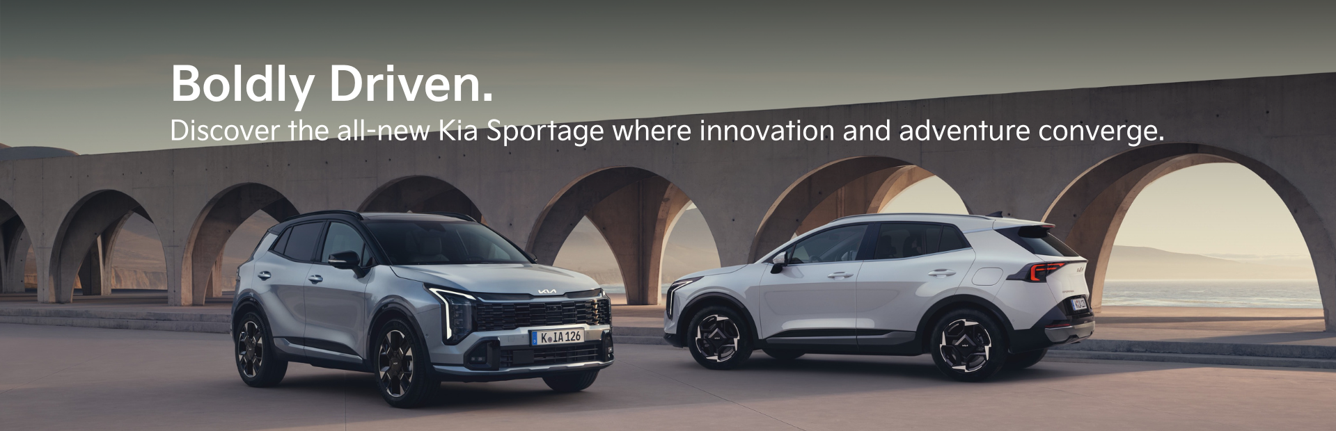 Two Kia Sportage cars parked in front of an arched concrete structure.